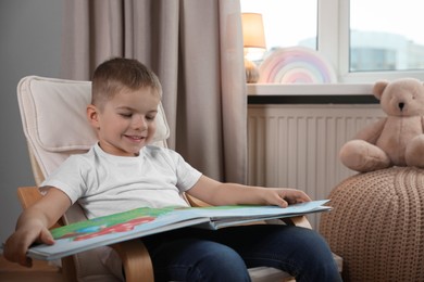 Photo of Cute little boy reading book at home, space for text