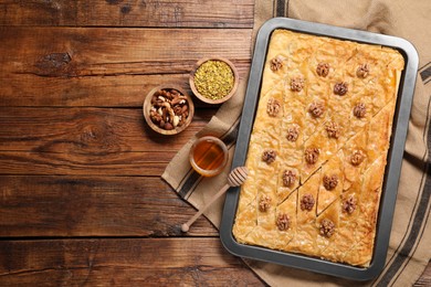 Photo of Delicious baklava with walnuts in baking pan, honey and nuts on wooden table, flat lay. Space for text