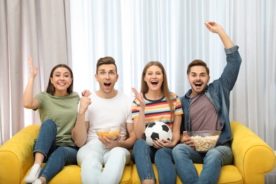 Photo of Group of people with snacks and ball watching soccer match on TV at home