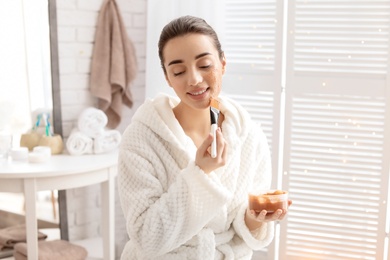 Photo of Young woman applying natural scrub on face in bathroom