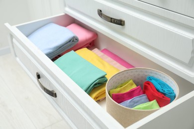 Photo of Chest of drawers with different folded clothes indoors, closeup