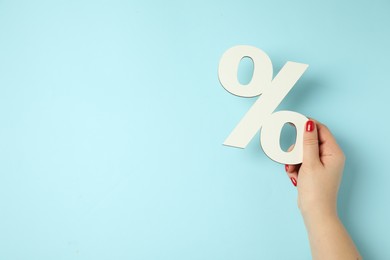 Photo of Woman holding percent sign on light blue background, closeup. Space for text