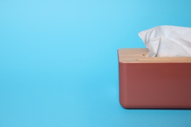 Photo of Holder with paper tissues on light blue background, closeup. Space for text