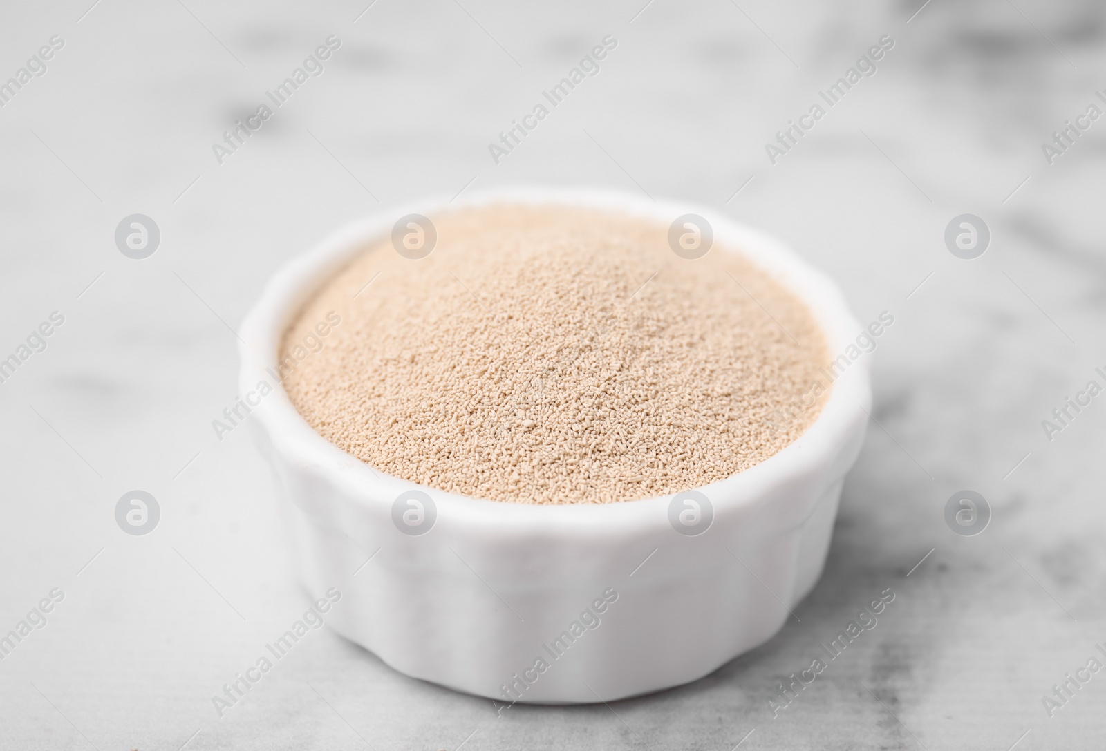 Photo of Granulated yeast in bowl on white marble table, closeup