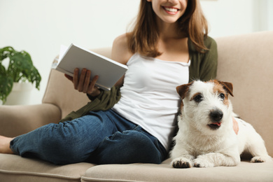 Photo of Young woman reading book and her cute Jack Russell Terrier on sofa at home. Lovely pet