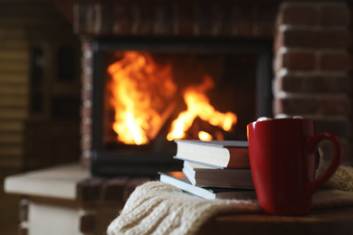 Photo of Books and cocoa on table near burning fireplace, space for text. Reading at home