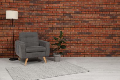 Photo of Cosy armchair, lamp and potted plant near brick wall in room, space for text. Interior design