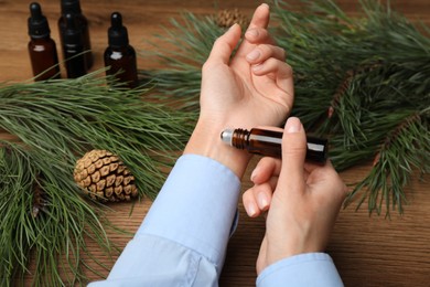 Photo of Woman applying pine essential oil on wrist at wooden table, closeup