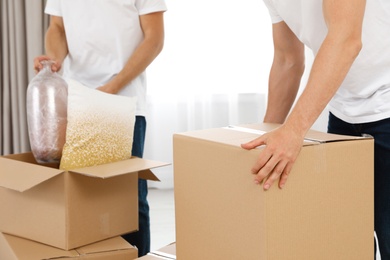 Photo of Moving service employees with cardboard boxes and belongings in room, closeup