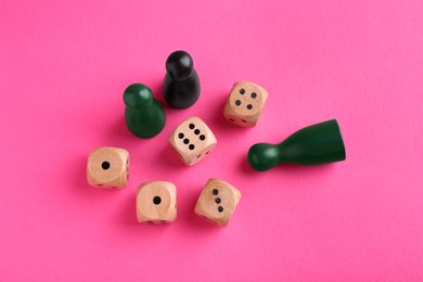 Photo of Wooden dices and color game pieces on pink background, flat lay