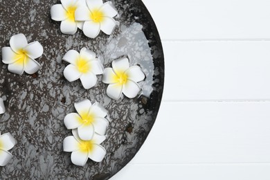 Photo of Bowl of water with plumeria flowers on white wooden table, top view and space for text. Spa treatment
