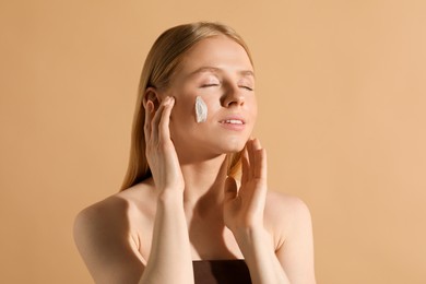 Photo of Beautiful young woman with sun protection cream on her face against beige background