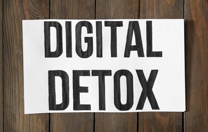 Photo of White paper sheet with words DIGITAL DETOX on wooden background, top view