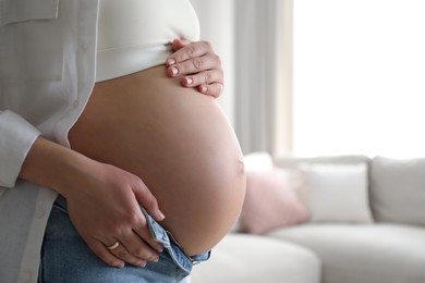Photo of Pregnant young woman touching belly at home, closeup. Space for text