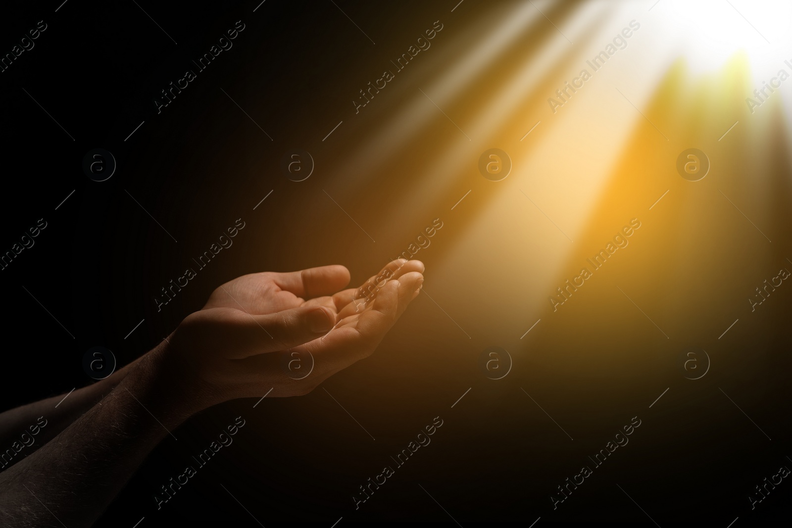 Image of Christian man stretching hands towards holy light in darkness, closeup. Prayer and belief