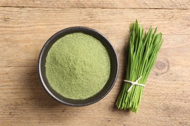Photo of Wheat grass powder in bowl and fresh green sprouts on wooden table, flat lay