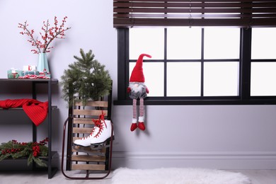Photo of Sleigh with pair of ice skates and fir branches near window in decorated room