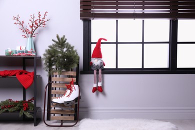 Photo of Sleigh with pair of ice skates and fir branches near window in decorated room