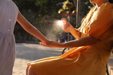 Photo of Mother applying insect repellent onto girl's hand outdoors, closeup