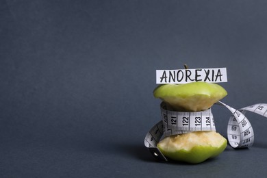 Photo of Apple core with measuring tape and word Anorexia on dark grey background, space for text
