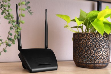 Photo of Modern wi-fi router and houseplant on wooden rack indoors