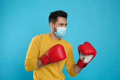 Photo of Man with protective mask and boxing gloves on light blue background. Strong immunity concept