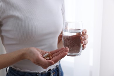 Photo of Woman with vitamin pills and glass of water indoors, closeup