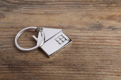 Photo of Metal keychain in shape of house on wooden table, closeup. Space for text