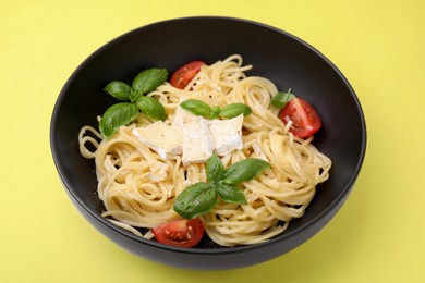 Photo of Bowl of delicious pasta with brie cheese, tomatoes and basil leaves on yellow background, closeup