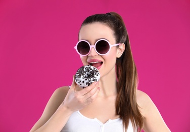 Photo of Beautiful young woman wearing sunglasses with donut on pink background