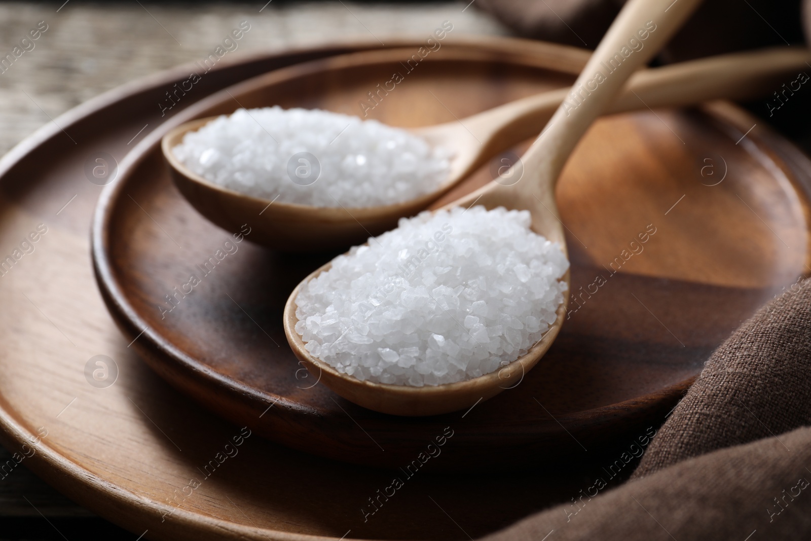 Photo of Organic salt in spoons on wooden table, closeup