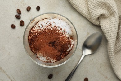 Photo of Delicious tiramisu in glass, spoon and scattered coffee beans on light table, flat lay
