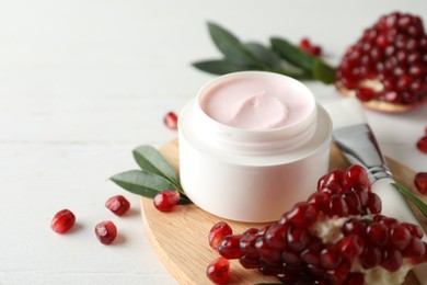 Photo of Jar with natural facial mask, pomegranate seeds and green leaves on white table, closeup