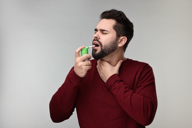 Photo of Young man using throat spray on grey background