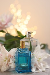 Photo of Bottle of perfume and beautiful lily flowers on table against beige background with blurred lights, closeup