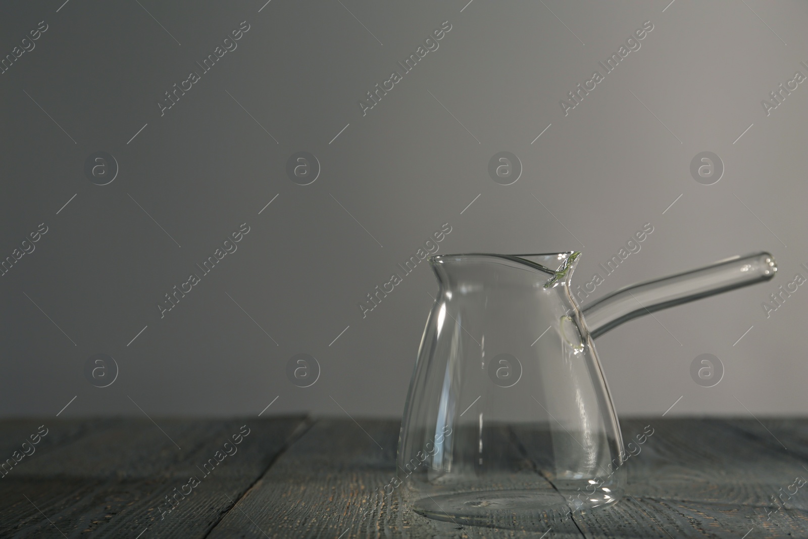 Photo of Empty glass turkish coffee pot on grey wooden table. Space for text