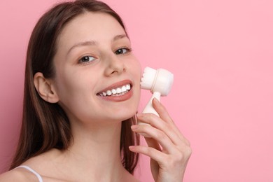 Photo of Washing face. Young woman with cleansing brush on pink background, space for text