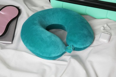 Photo of Turquoise travel pillow, suitcase, sleep mask and earphones on bed