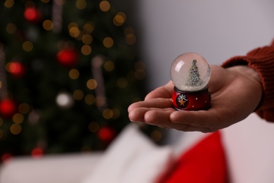 Photo of Man in warm sweater holding snow globe indoors, closeup