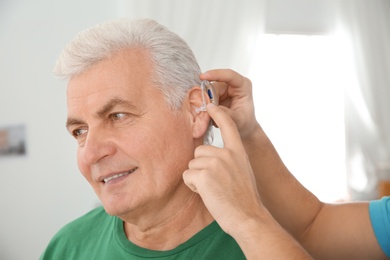 Photo of Young man putting hearing aid in father's ear indoors