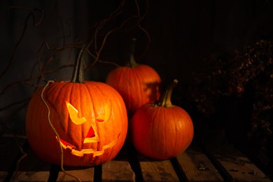 Photo of Scary jack o'lantern pumpkin on wooden bench in darkness, space for text. Halloween decor