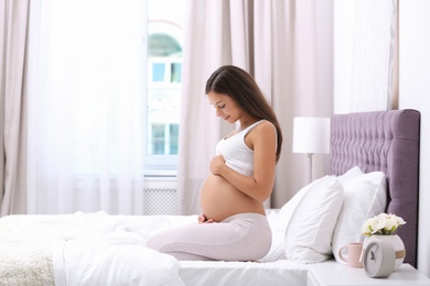 Photo of Happy pregnant woman sitting on bed at home