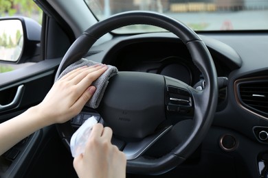 Photo of Woman cleaning steering wheel with rag in car, closeup