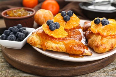 Fresh tasty puff pastry with sugar powder, jam, tangerines and blueberries on wooden table, closeup