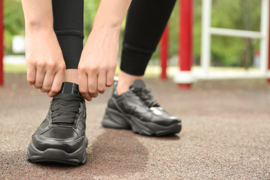 Woman tying laces of stylish sneakers outdoors, closeup