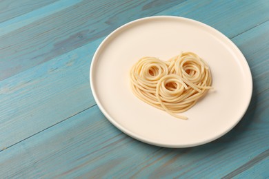 Photo of Heart made of tasty spaghetti on light blue wooden table. Space for text
