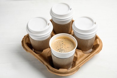 Photo of Takeaway paper coffee cups with sleeves in cardboard holder on white wooden table