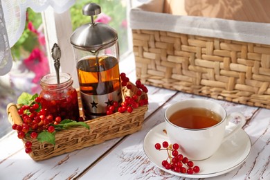 Photo of Cup of hot drink and viburnum berries on white wooden table indoors