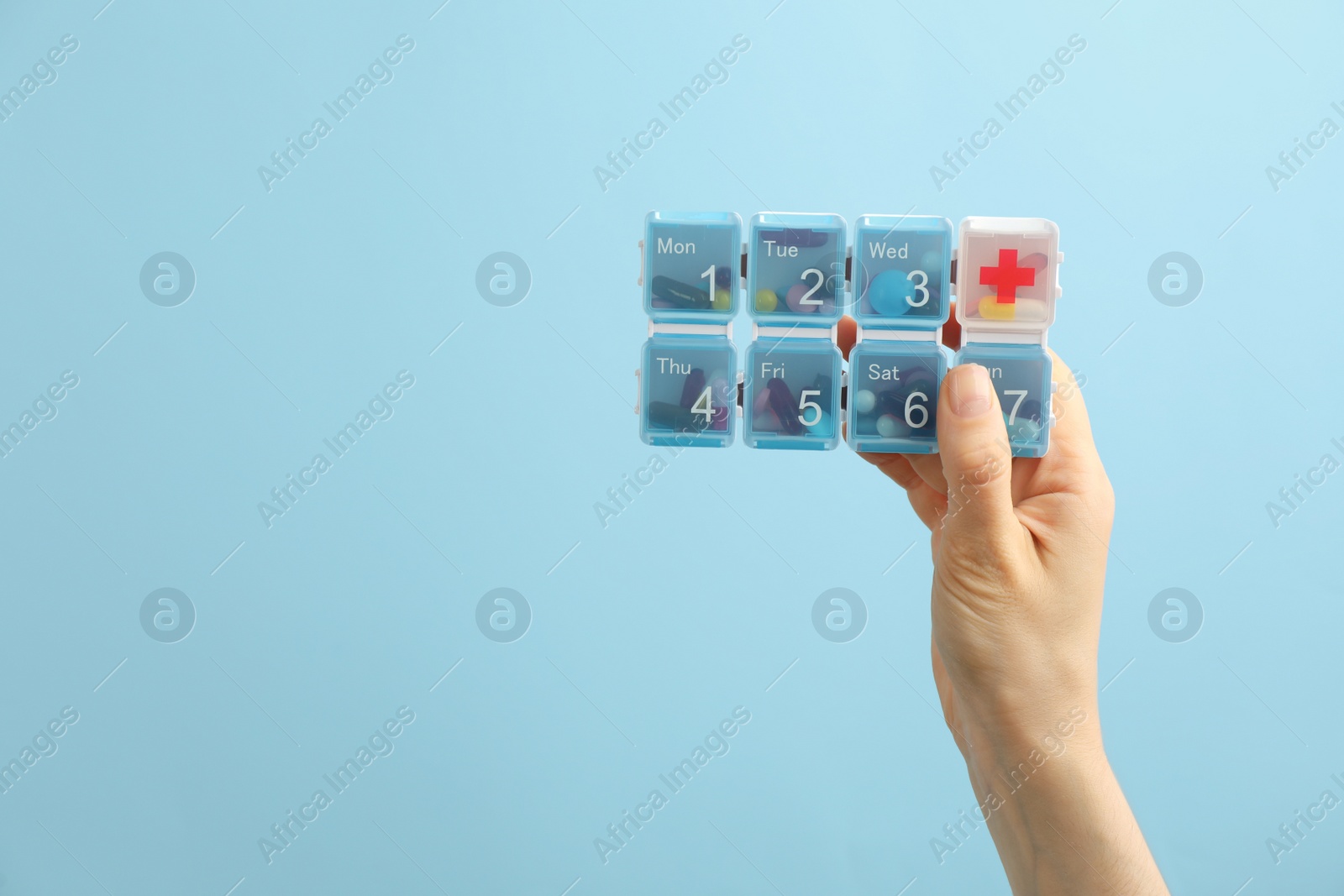 Photo of Woman holding plastic box with different pills on light blue background, closeup. Space for text