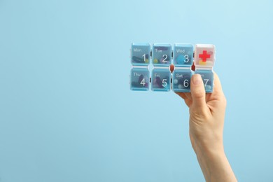 Photo of Woman holding plastic box with different pills on light blue background, closeup. Space for text